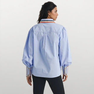 Woman wearing a light blue shirt with colorful collar and cuffs on a beige background