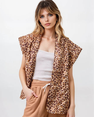 Woman wearing a leopard print vest over a white top and beige pants on a white background