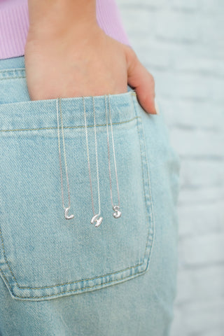Three gold letter necklaces styled against light wash denim