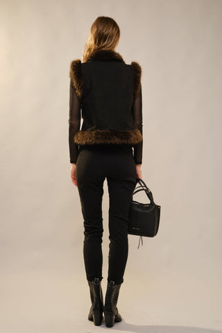 Person wearing a black outfit with fur details on a plain background
