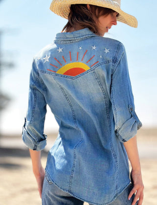 Person wearing a denim shirt with a sun and star design on a beach.