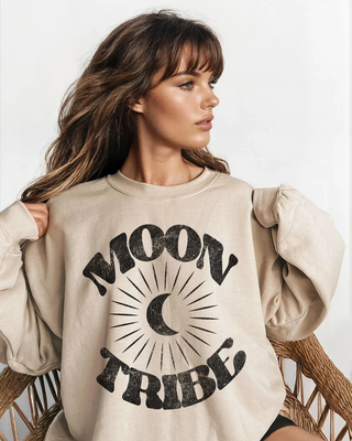 Woman wearing a beige sweatshirt with 'Moon Tribe' text, sitting on a wicker chair.