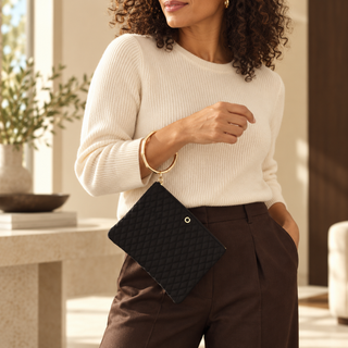 Woman wearing the black quilted Big O bracelet pouch hands-free with cream knit and chocolate trousers