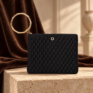 Black quilted Big O bracelet pouch with gold circular handle on cream stone