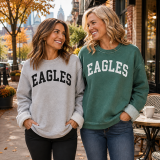 Two women wearing grey and mineral green Eagles sweatshirts in a fall city setting