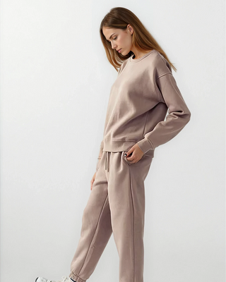 Woman wearing a beige tracksuit with white sneakers on a light gray background
