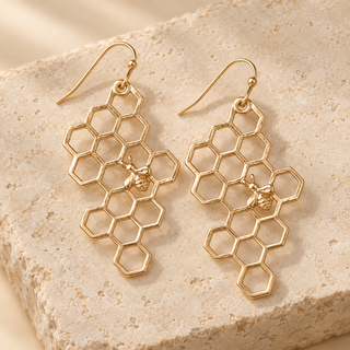 Pair of gold honeycomb bee statement earrings styled on warm cream stone