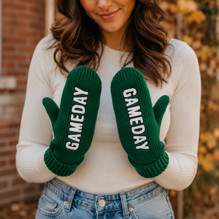 Woman wearing forest green ribbed knit mittens with white vertical GAMEDAY lettering in a warm fall setting.