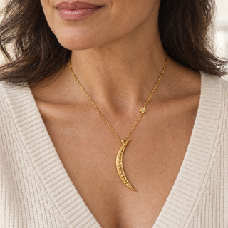 Luna & Light gold crescent moon necklace worn with a cream V-neck knit, showing the statement pendant and small star accent.