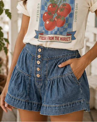 Woman wearing a 'Tomato Season' t-shirt and straw hat on a porch with tomato plants.