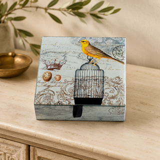 Yellow Bird and Cage Glass Keepsake Box displayed on a warm cream console